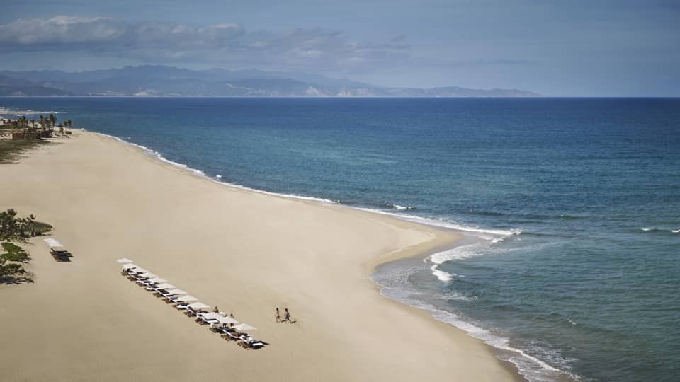 a large white-sand beach with a row of white umbrellas and lounge chairs
