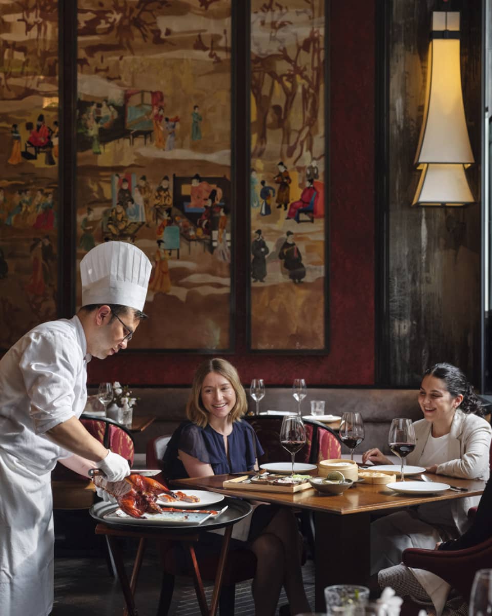 Two women being served food by a chef.