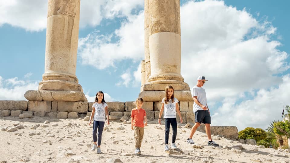 A parent and three children walk together next to the ruins of the Amman Citadel