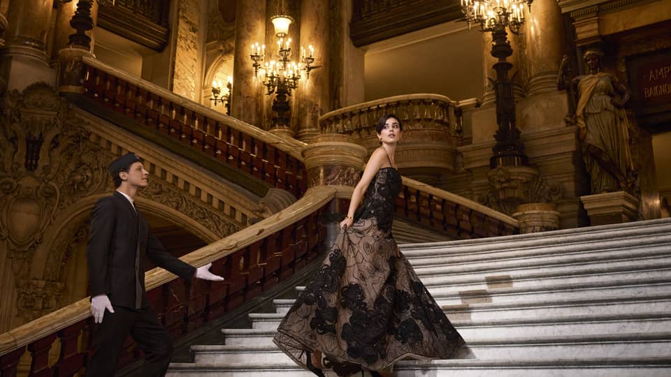 A woman in ballgown ascends grand staircase of opera