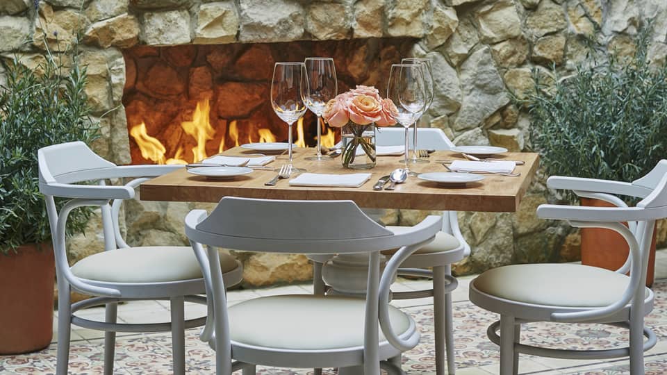 Close-up of white chairs and dining table set with wine glasses, flowers, in front of brick fireplace  