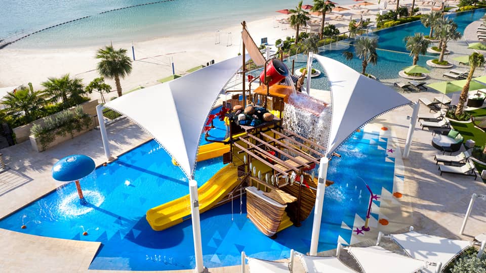 A large orange waterslide built into a faux pirate ship descending into a crystal blue pool of water.