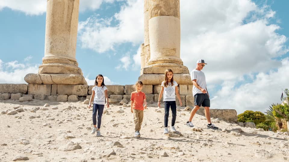 A parent and three children walk together next to the ruins of the Amman Citadel