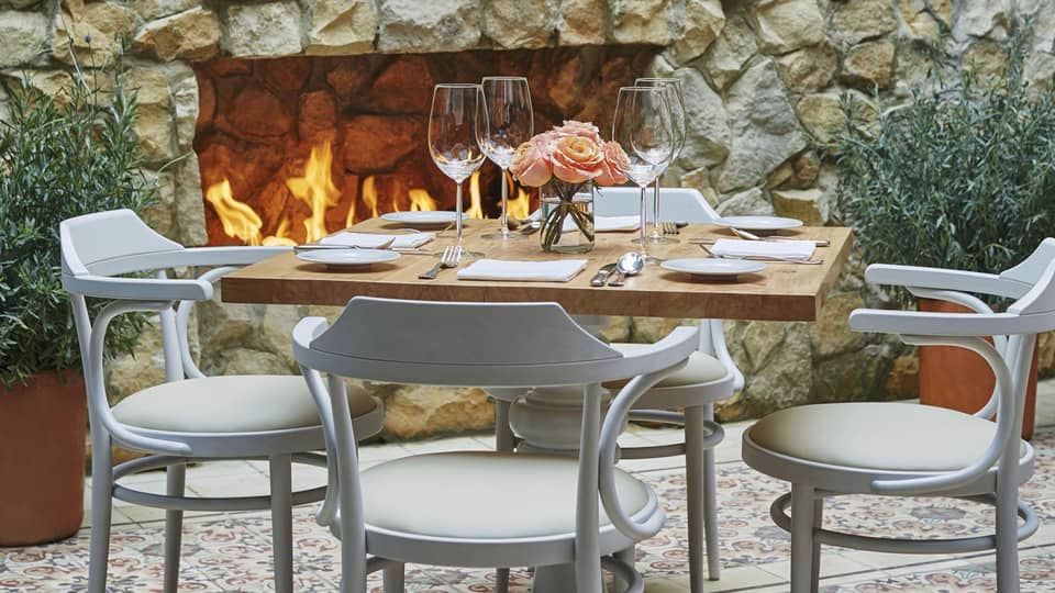 Close-up of white chairs and dining table set with wine glasses, flowers, in front of brick fireplace