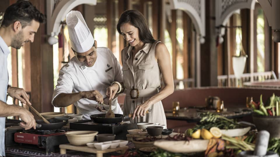 A chef is instructing a man and woman in the Ikan Ikan Cooking Class