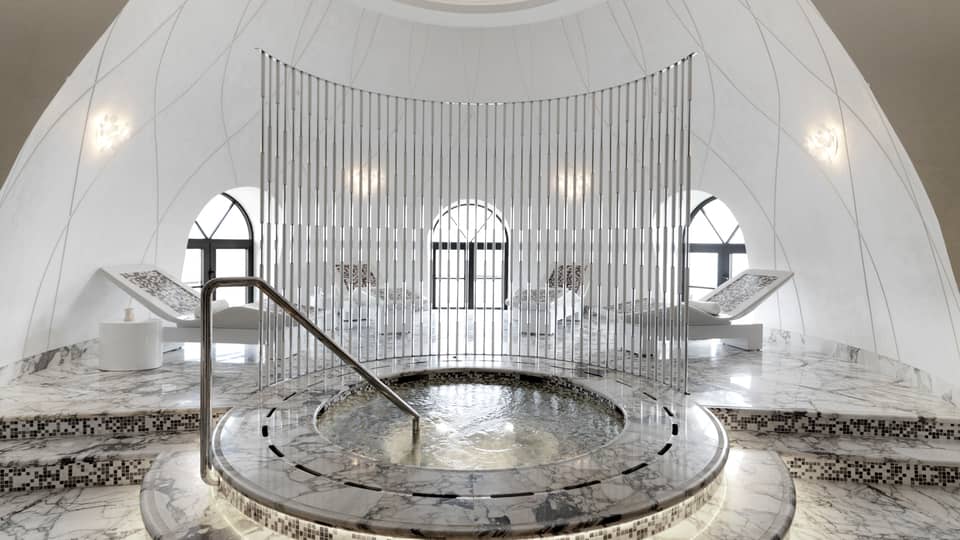 Round spa tub with black-and-white marble and tiles in middle of white dome room