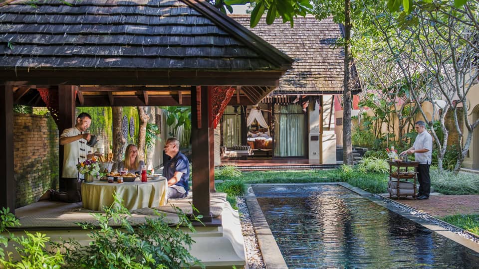 Hotel staff serve couple under dining gazebo by pond 