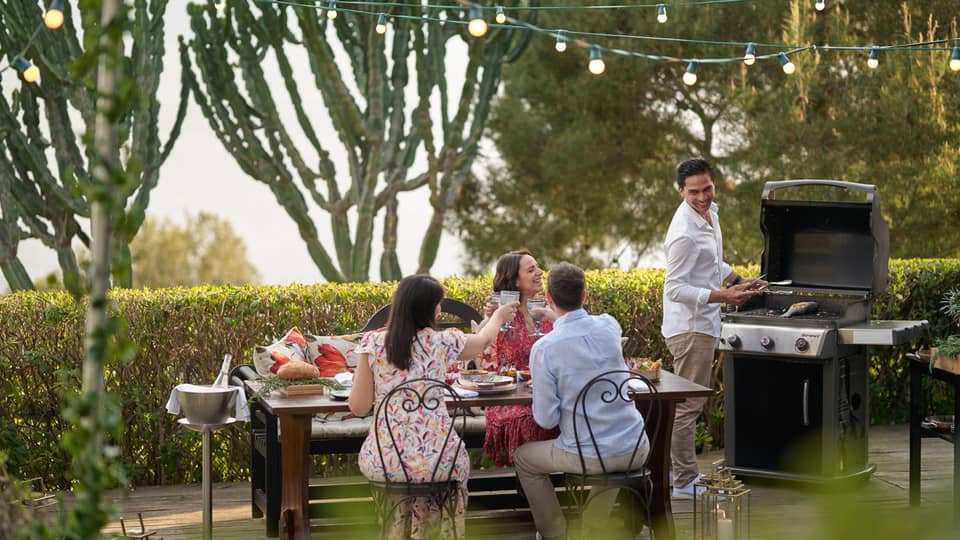 A group of four people grilling food outside at a large table while wearing nice beach clothes.