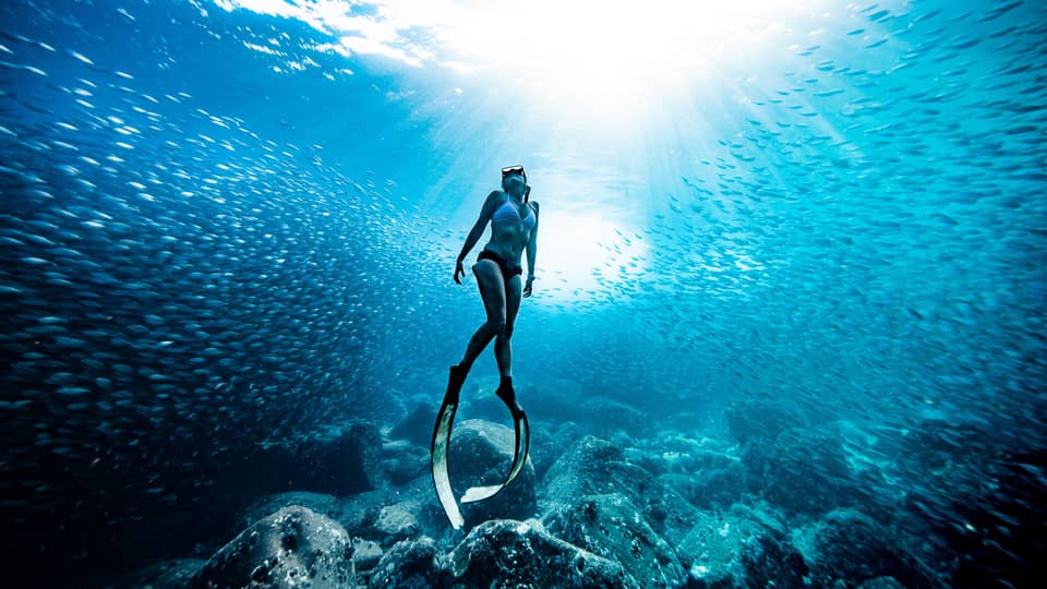 A woman in bikini wears scuba slippers below the surface of the ocean water
