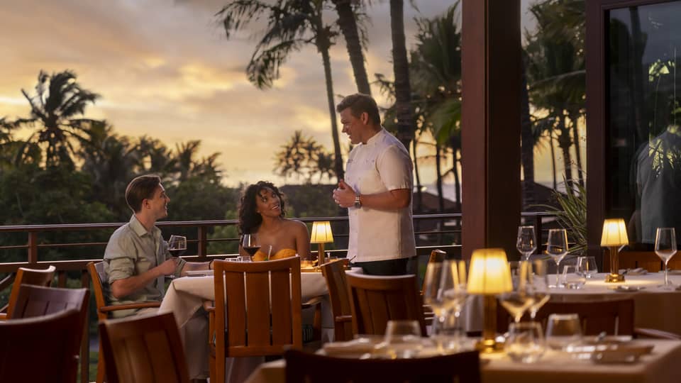 Chef Tyler Florence speaks to man and woman dining at outdoor Miller and Lux Hualalai restaurant