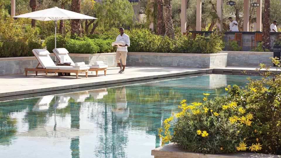 Server holding folded towels walks by lounge chairs, umbrella by adults-only outdoor swimming pool