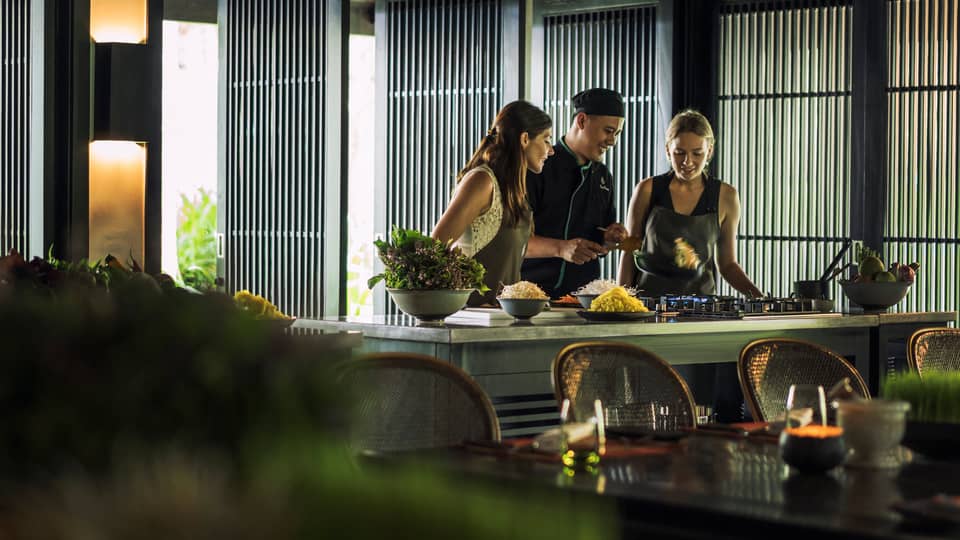 Chef, two women look at pan on kitchen range at Hoi An Cooking Academy 