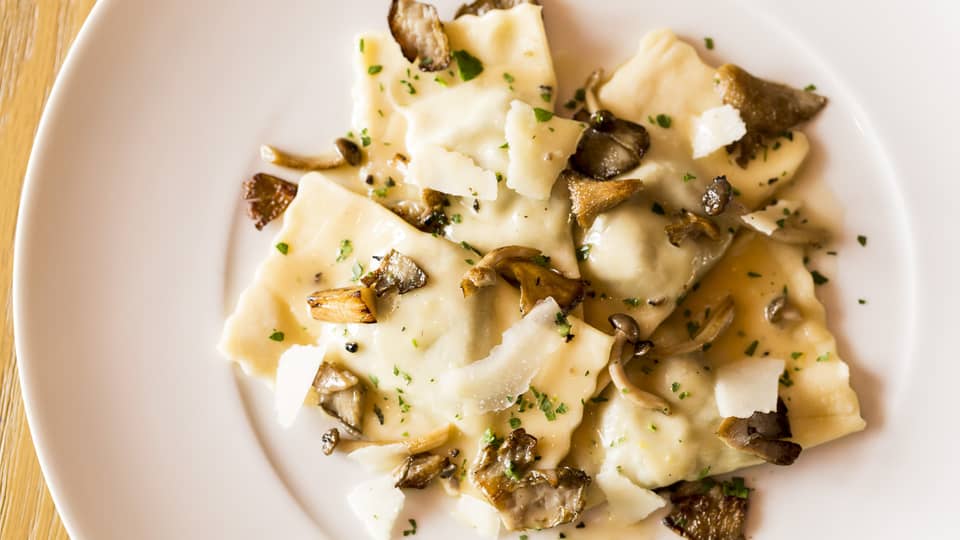 Veal Ravioli pasta garnished with shaved parmesan cheese, mushrooms on plate