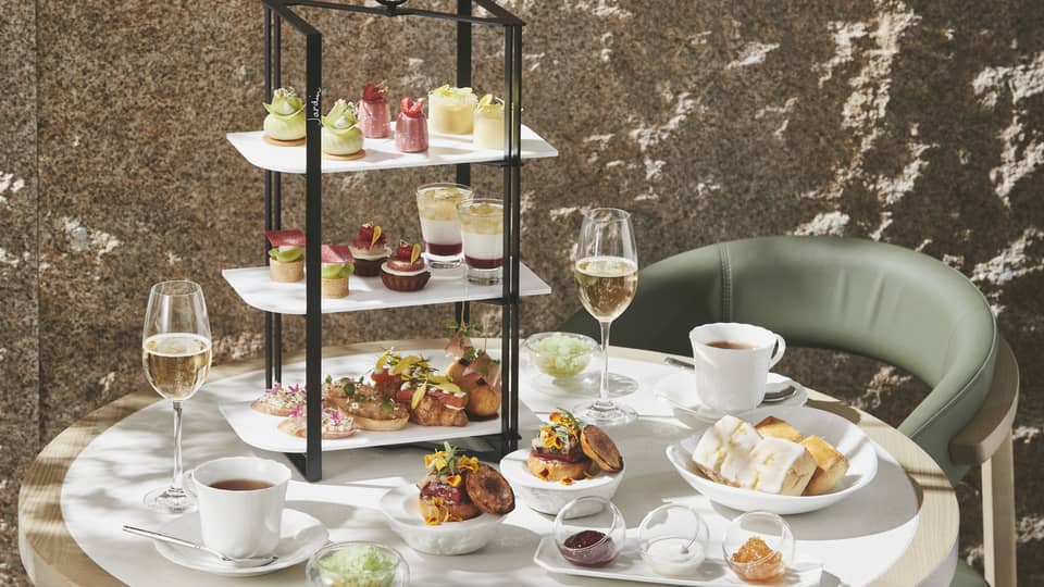 Afternoon Tea set up with three-tiered display of sweet and savoury foods, two glasses of champagne and two glasses of tea
