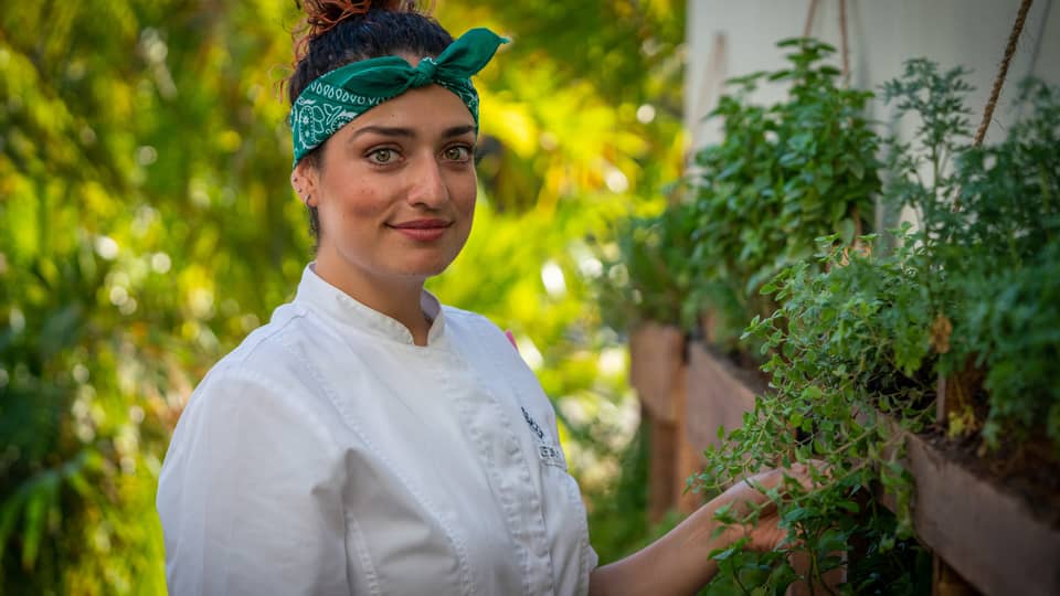 A female chef in a green bandana looking at herbs.