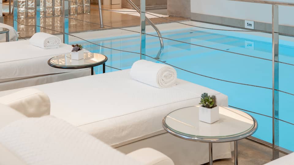 A spacious, well-lit indoor pool area with comfortable poolside spa treatment tables