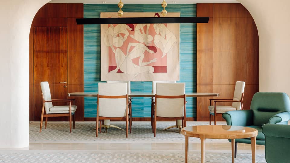 Elegant dining area with a long table, white chairs, colorful wall art and wood-paneled walls framed by an arched entryway.