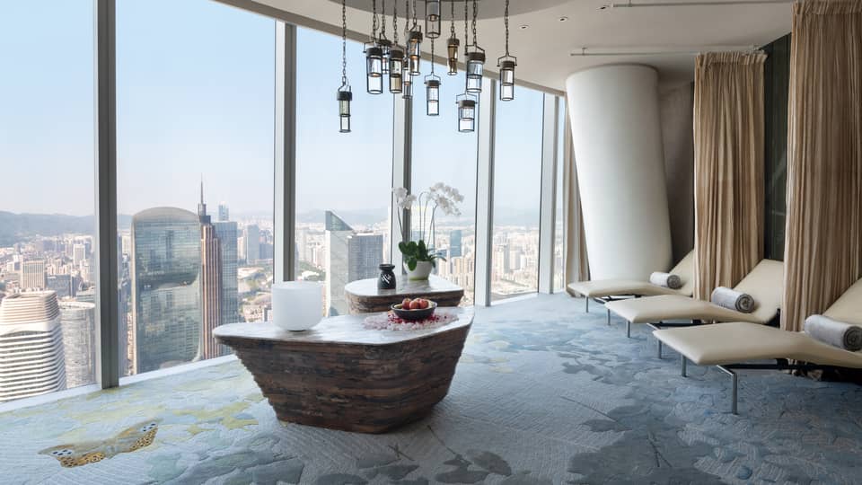 Large soaking tub filled with flower petals overlooking the cityscape from floor-to-ceiling windows