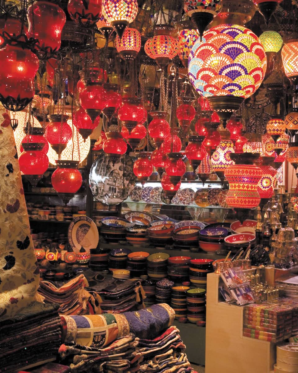 Red lanterns hang over shelves with decorative plates in Grand Bazaar