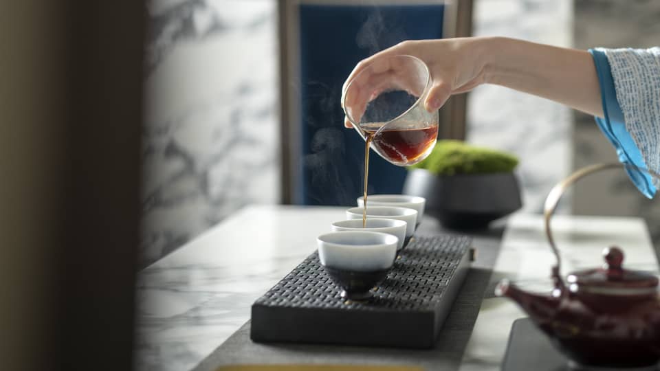 Woman's hand pours tea into mugs for traditional tea ceremony