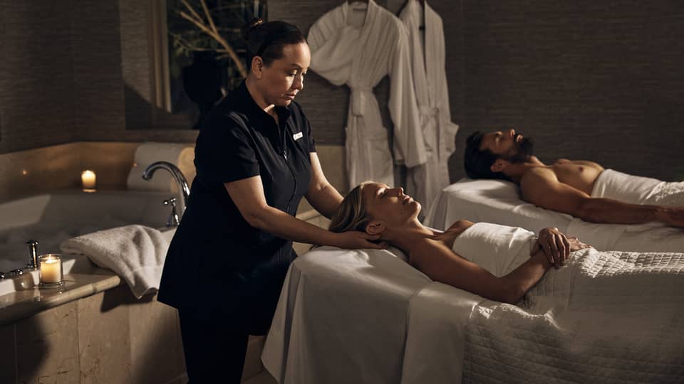 Two guests laying on massage tables in a room with a spa tub.
