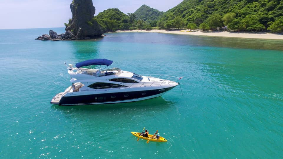 Two people in yellow kayak in front of large white yacht by island in blue ocean