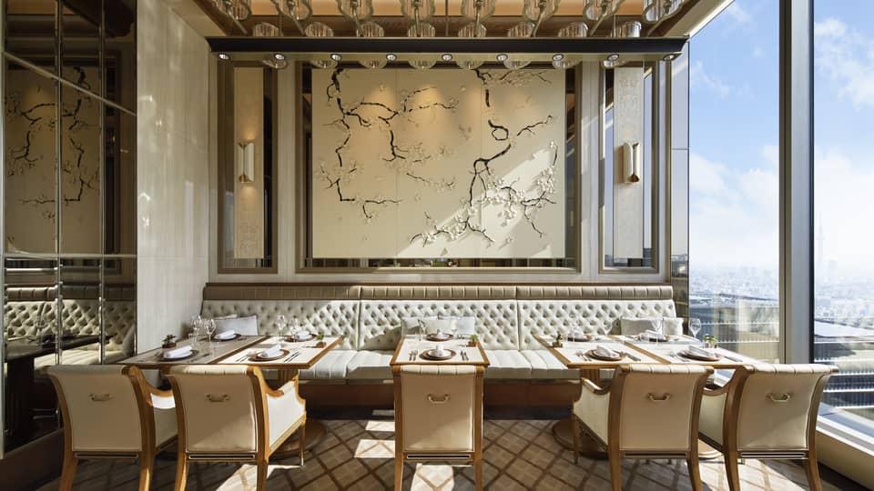 Est dining room with tables for two, muted cream decor, natural light, view of the city 