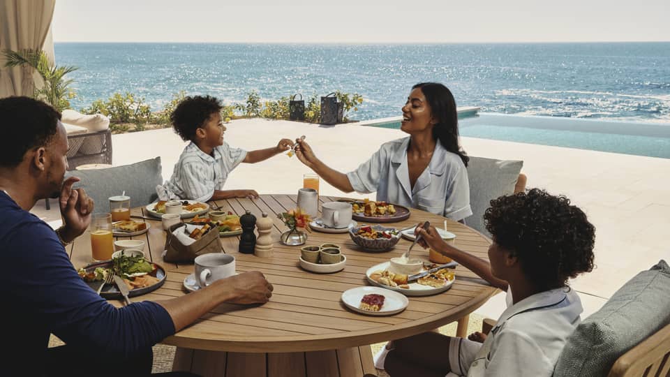 Family enjoying breakfast together at a round wooden table on an ocean-view terrace at a luxury resort