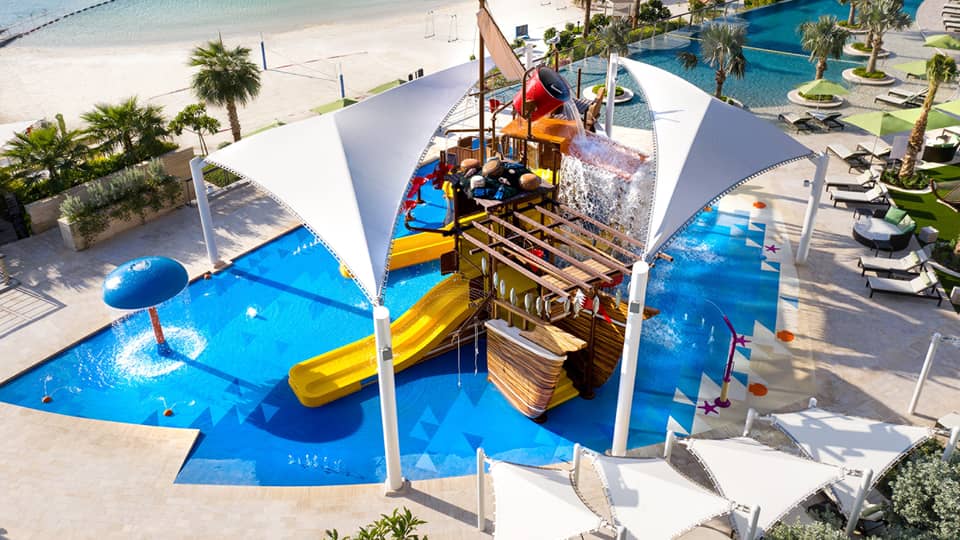 A large orange waterslide built into a faux pirate ship descending into a crystal blue pool of water.
