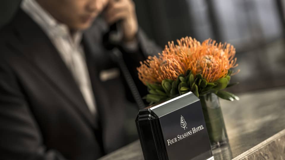 Close-up of Four Seasons Hotel concierge desk, orange flowers in vase, staff on phone