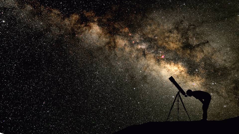 Silhouette of stargazer leaning into telescope against a starry sky, milky way