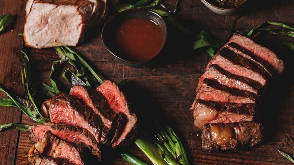 A aerial view of the La Hiki Steak over green onions with a red sauce on the side