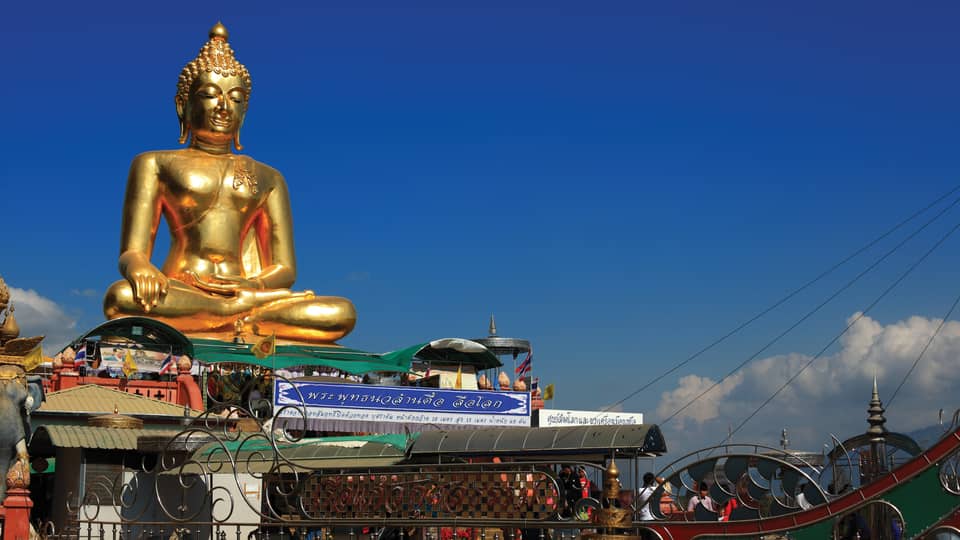Gold Buddha statue on temple roof against a blue sky