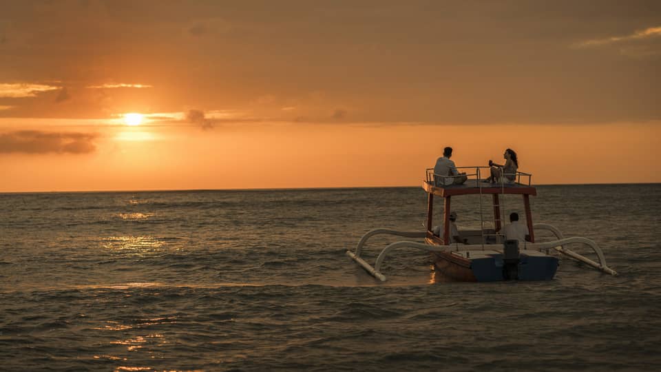Sunset cruise boat on water under orange sky