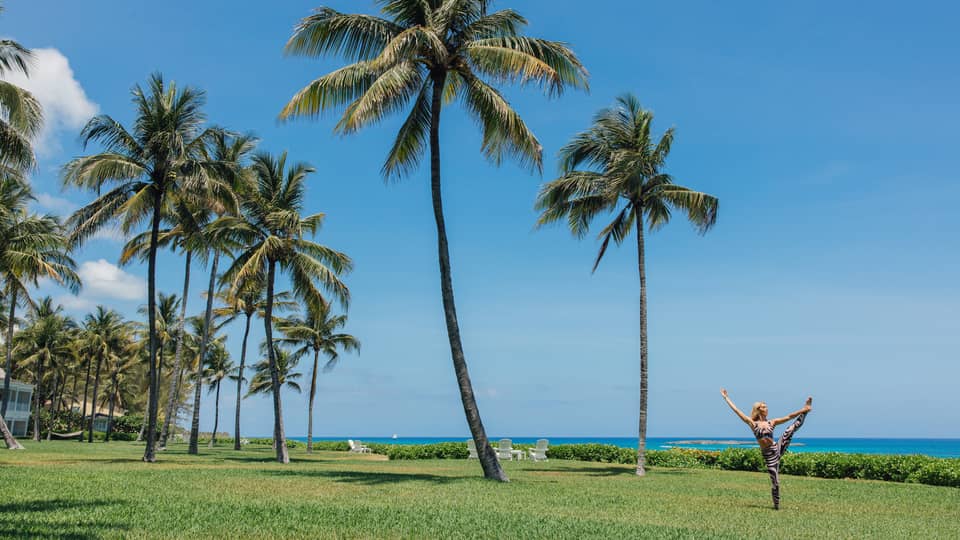 A person doing a yoga pose outside near the ocean and palm trees