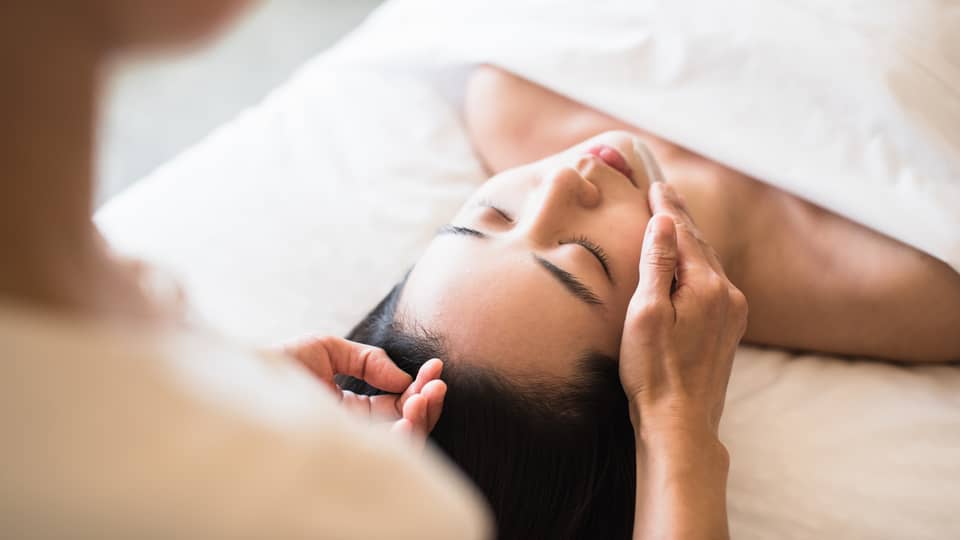 A guest receiving a soothing facial at a spa, lying on a massage table, surrounded by calming décor and soft lighting.