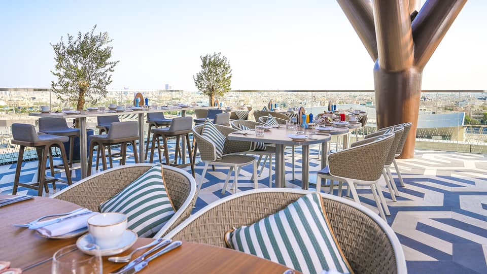 Elements' outdoor patio outfitted with rattan chairs, wood tables and a blue-and-white patterned floor, all overlooking the park with the city in the distance
