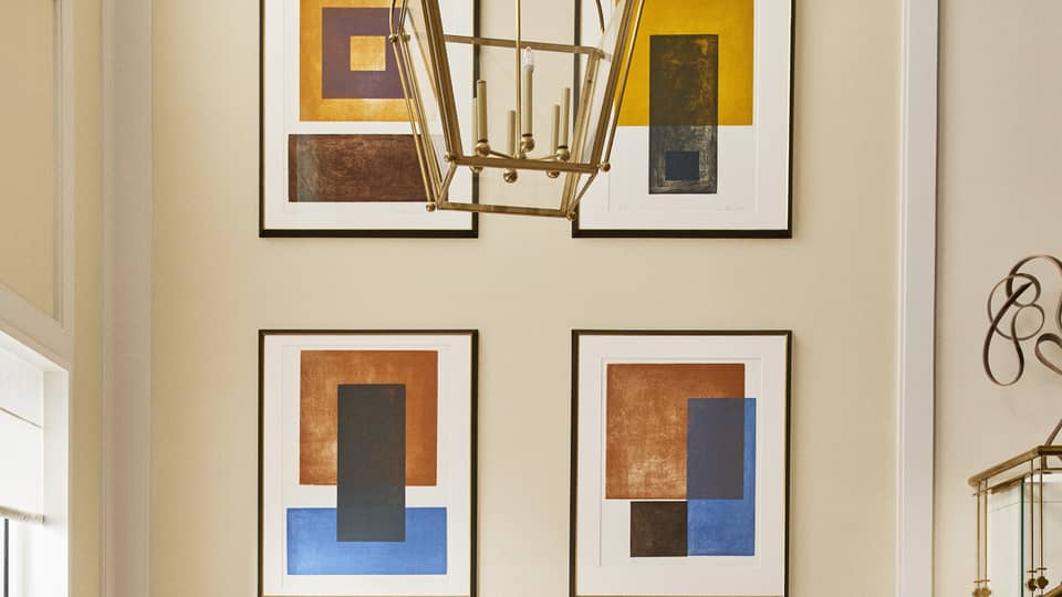 Luxury hotel seating area with a white round table and tan upholstered chairs beneath a chandelier, featuring abstract framed artwork on the wall 