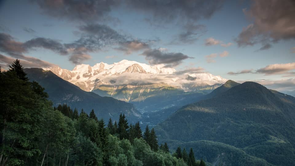 Clouds, sunshine over ice-capped French Alps behind green mountains