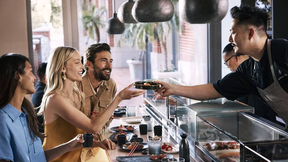 Three guests sitting at a table while the chef serves their food.