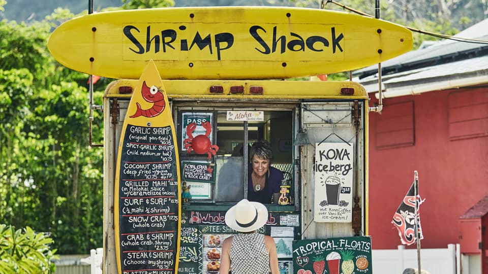 Woman orders from Shrimp Shack food stand with colourful yellow signs 