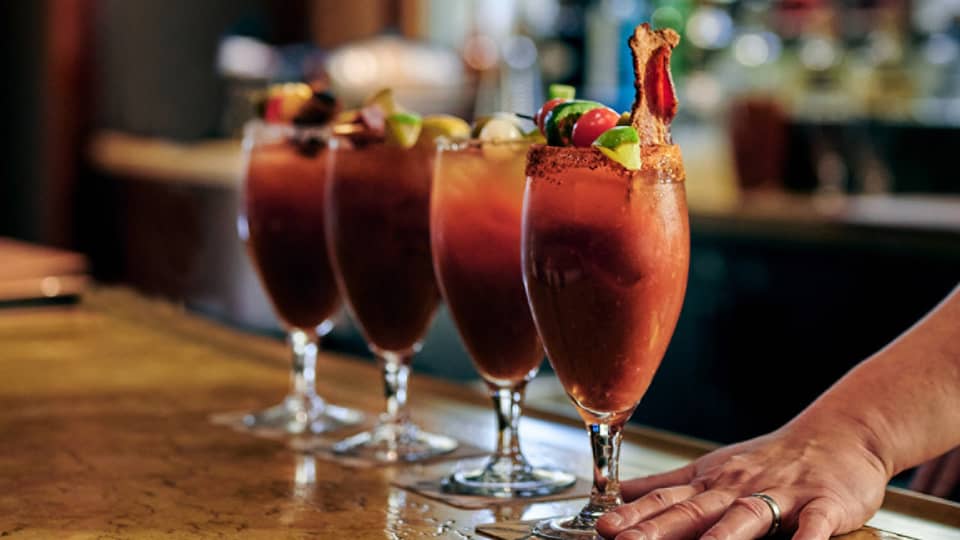 ,A bartender serves up four bloody marys at a bar