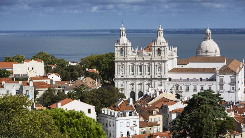White cathedrals, houses and rooftops in Lisbon, ocean in background
