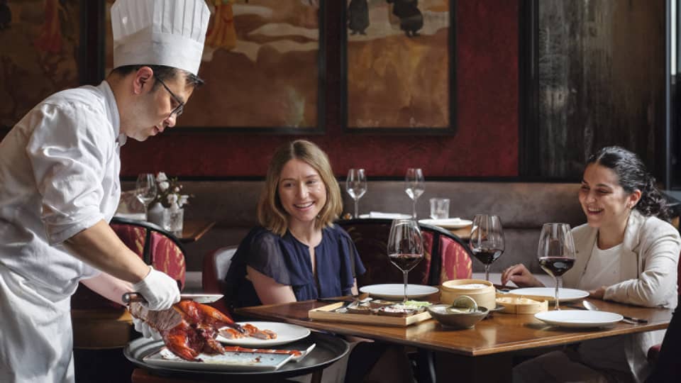 Two women being served food by a chef.