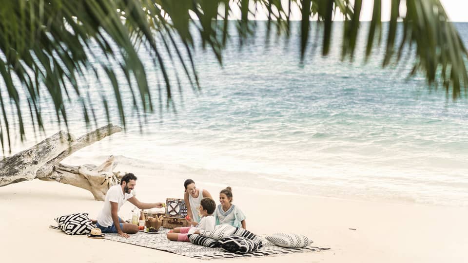 A man, woman and two children picnic on the beach just a couple feet away from the ocean. 
