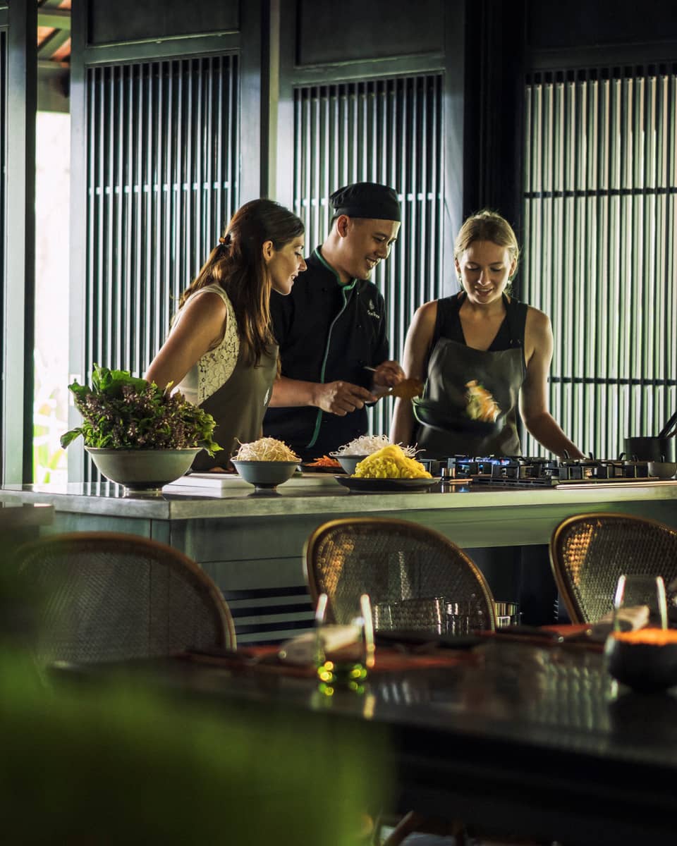 Chef, two women look at pan on kitchen range at Hoi An Cooking Academy 