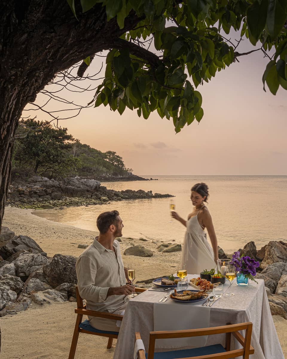 A beach dinner date at dusk, with a couple enjoying a serene seaside view.