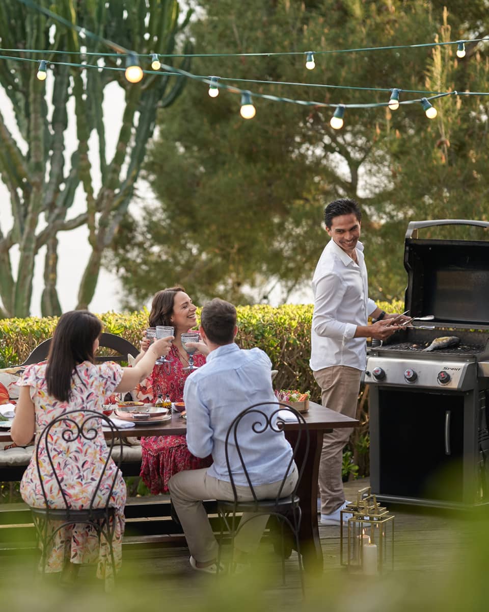 A group of four people grilling food outside at a large table while wearing nice beach clothes.