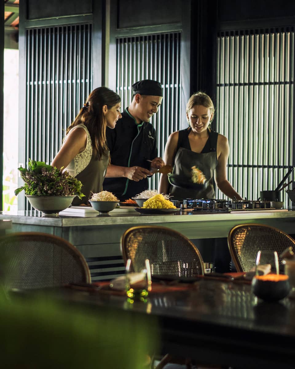 Chef, two women look at pan on kitchen range at Hoi An Cooking Academy 
