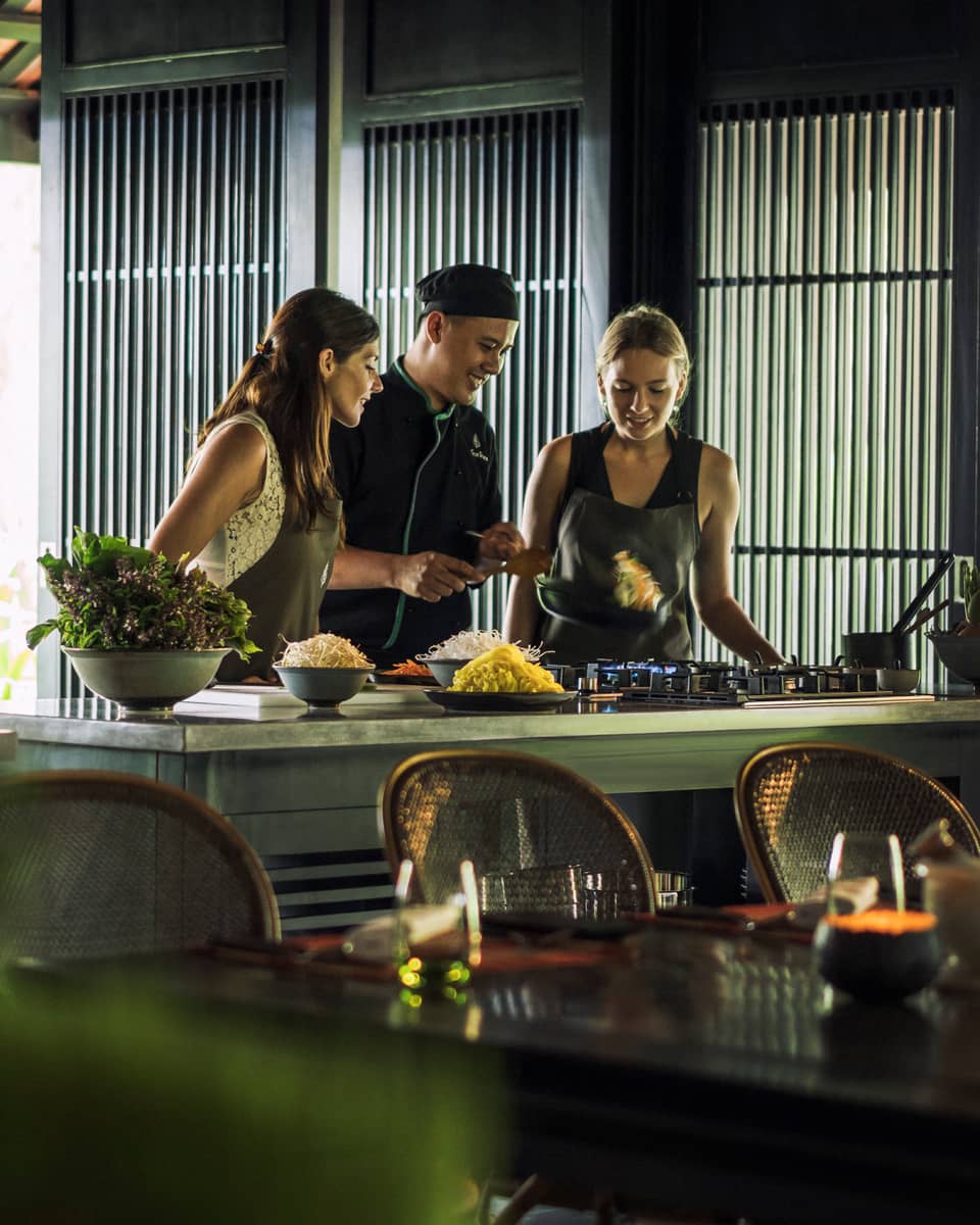 Chef, two women look at pan on kitchen range at Hoi An Cooking Academy 
